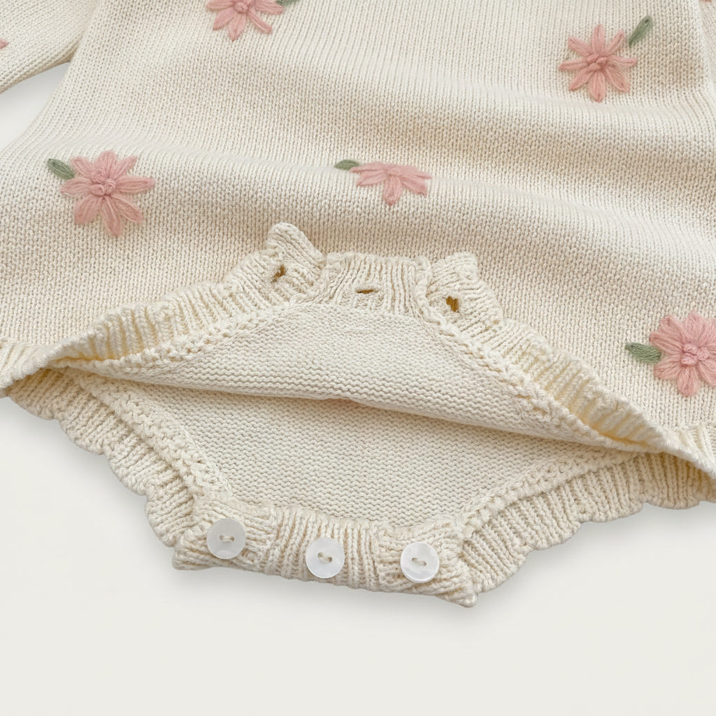 Cream-colored baby outfit with floral embroidery on a textured surface